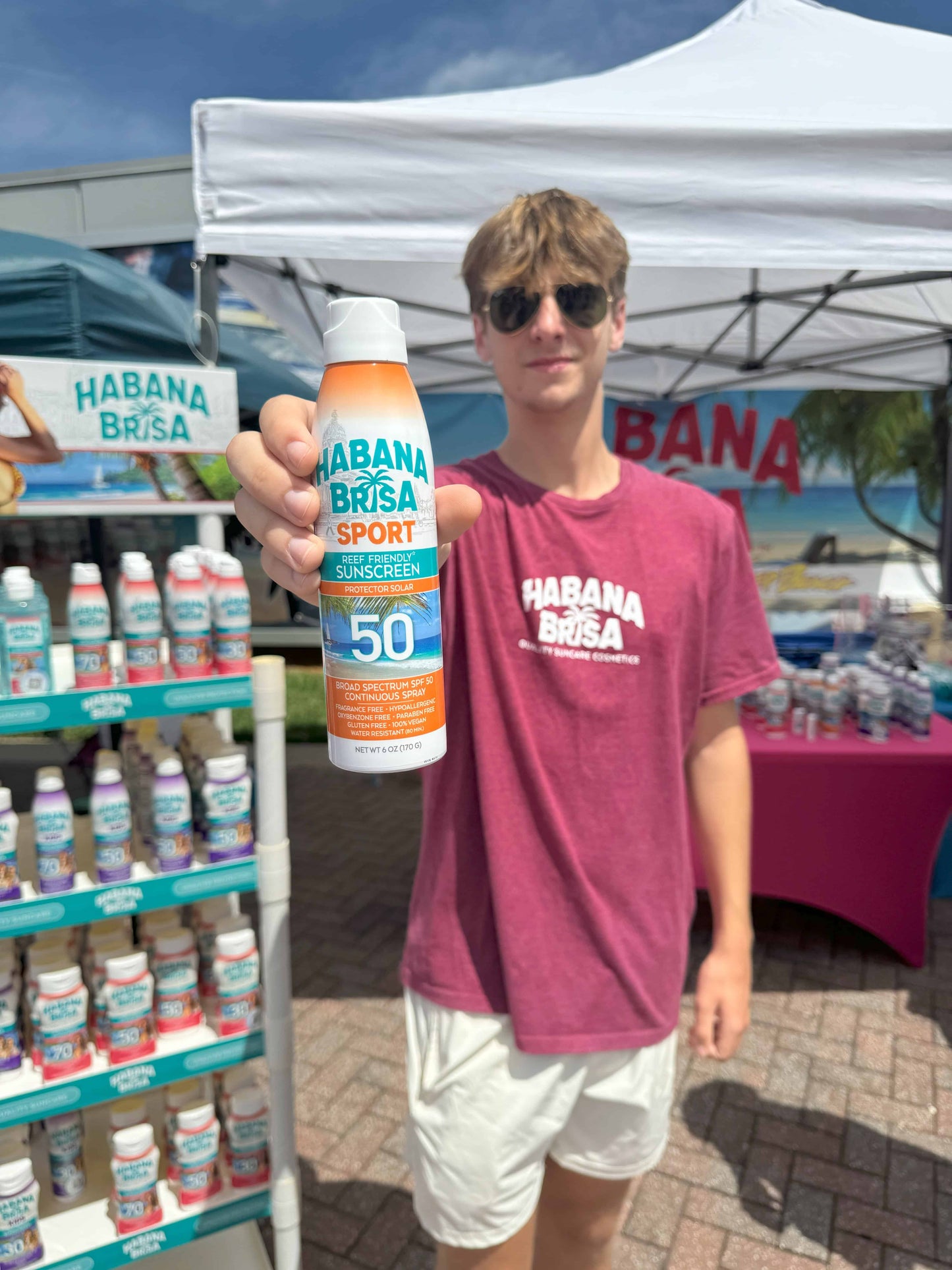 Young athlete holding Habana Brisa Sport Sunscreen SPF 50 at outdoor event booth, highlighting reef-safe, sweat-resistant sun protection
