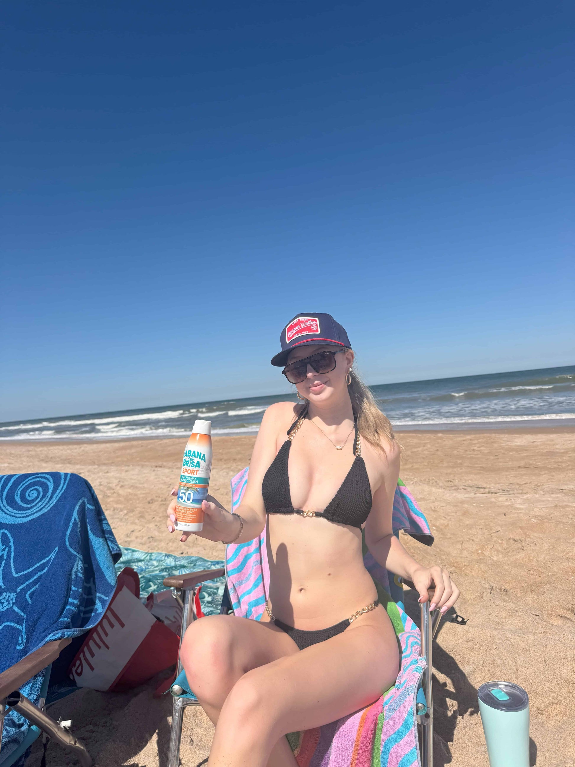 Woman in black bikini holding Habana Brisa Sport SPF 50 sunscreen on sunny beach